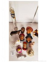 Top-down view of the lot showing the tall old style glass thermometer and an assortment of colorful ceramic face wall plaques and various white porcelain figurines.