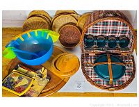 Overview of entire lot showing picnic basket with tableware, punch bowl, lazy Susan, placemats, cutting board and utensils