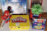 Wide shot showing Play Mobile castle set box, Play-Doh set, toy shopping cart with green toy plant, and Martian Matter Master game box