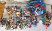 Top-down photo showing multiple clear plastic bags filled with various small plastic toys including animals, figures, and toy vehicles spread out on a floor surface