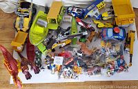 Overhead view of a large assortment of toys including multiple vehicle toys, animal figures, and various action figures on a white background.