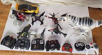 Wide view of assorted remote control toys including cars, helicopters, drones and robotic dinosaur with their controllers.
