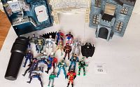 Overview of DC Batman action figures and 1990s Batcave playset arranged on white backdrop, showing figures and playset building pieces.