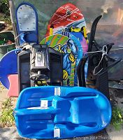 Snow sleds and snowboards arranged upright showing different sizes and styles including the original GT Snoracer sled and Blizzard snowboard.