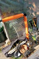 Orange lacrosse goal with net, lacrosse sticks, baseball gloves, helmet, and catchers mask on sidewalk outdoors