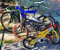 Photo showing three bicycles together: blue Jeep brand, black/red bike, and yellow children's bike with training wheels.