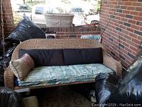 Front view of wicker porch swing with cushions and decorative pillows on covered porch.
