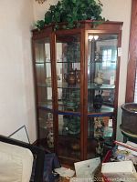 Front view of tall wooden lighted corner display case with glass shelves and multiple decorative ceramic and glass items inside