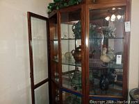 Wide view of wooden-framed glass cabinet displaying tea pots, glassware, and figurines.