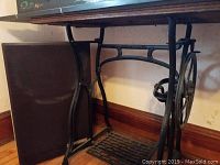 Side angle of Wheeler and Wilson pedal sewing machine stand showing cast iron base with wheel mechanism and wooden parts.