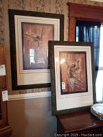 Two framed Mona Stewart paintings hanging on wall and standing on furniture, both feature abstract dancing figures in earthy tones with textures