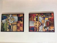 Two small framed art prints depicting chefs in kitchen scenes with colorful cartoon style and brown frames.