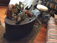 Full view of oval metal wrapped coffee table with decorative items on top, alongside industrial style stool with cream vinyl seat on wheels.