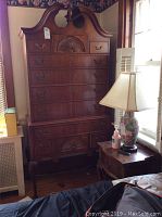 Front view of tall Thomasville highboy chest of drawers showing bonnet top, carved shell details and brass handles.