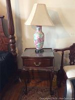 Matching Asian-inspired ceramic table lamp with floral shades placed on Empire brand wooden night stand with glass protective top.