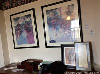 Two large abstract artworks with black frames hanging on the wall, accompanied by smaller framed artworks on a surface below, showing condition of frames and art.