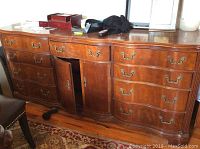 Full front view of medium brown wooden dresser showing ten drawers with bow front design and central cabinet door with aged brass-tone handles.