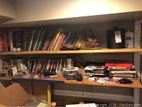 Shelf with assorted DVDs in cases and stacked books. DVDs unpackaged as noted by seller.