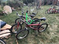 Three children's bikes with flat tires arranged outdoors, on patchy grass with other yard furniture and bikes in the background.