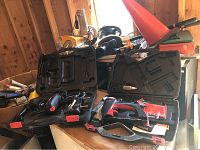 Photo of several power tools on a table including two cordless drills, a rotary trim cutter, buffer, and table saw in the background