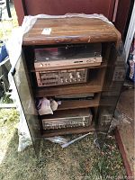 Wooden stereo cabinet with two glass doors open showing multiple audio components inside.