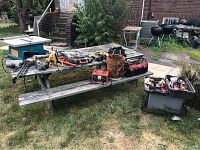 Various power tools and hand tools arranged on a picnic table and on the ground, showing the overall lot including drills, nailer, toolboxes, and tool bucket.