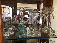 Photo of assorted glass candlesticks on mirrored shelf showing multiple styles and sets.