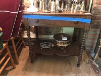Front view of the antique wooden tea table showing drawer with knobs, spiral turned legs, the heart-shaped scalloped shelf near the base, and some items placed on top and below.