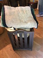 Photo of vintage wooden magazine rack holding folded throws, showing vertical slats and cut-out handles