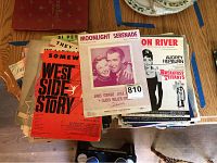 Photo showing a stack of vintage piano sheet music, featuring prominent covers of West Side Story, Moonlight Serenade from The Glenn Miller Story, and Breakfast at Tiffany's.