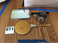 Two vintage hand mirrors and a stainless steel cup on wooden table