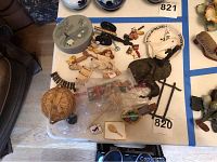 Overview of lot with brass cannon, doll, basket, box, and ornaments on white surface with blue tape.