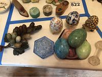 View of all items showing marble grapes centerpiece, pink depression glass bowl with five marble eggs, blue hexagonal glass dish, and three decorative eggs on stands