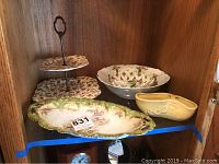 Shelf display with all items: two-tier floral serving piece, oval bread dish, yellow flower holder, porcelain basket bowl, floral bowl