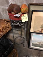 Pedestal table with wicker top and decorative metal legs, red metal tin on top, and wooden shoes resting on tin lid