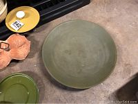 Photo shows a large olive green ceramic serving platter and other serveware pieces placed on a surface