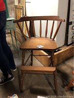 Vintage wooden high chair with spindle back and worn left arm visible, showing natural wood finish and sturdy legs