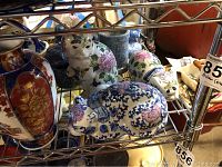 Porcelain cat figurines with floral designs alongside other ceramics on metal shelf
