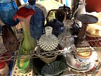 Photo showing tall chicken vase, various blue and clear glass vases, metal candle holder, and blue ceramic teapots on metal shelving rack