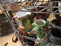 Floral ceramic pitchers and small pottery bowls and cups on metal shelf