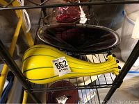 Yellow gourd-shaped art glass piece with black stripes, about 13 inches long, placed on metal shelf in basement.
