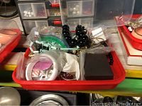 Tray of assorted costume jewelry featuring black bead necklace, white and pink bangles, and other pieces in plastic bin