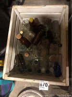 Overview of wooden crate containing various antique and vintage glass bottles and decanters in clear, brown, and cobalt blue glass.