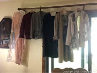 Photo showing eight hanging garments on a rod including a peach transparent peignoir, maroon jacket, gray jacket, black dress, beige dress, black dress with beaded sheer upper bodice, cream trench coat, and a beige garment.