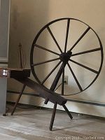 Full view of the antique wooden spinning wheel showing large wheel and supporting bench.