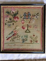 Full view of framed antique sampler showing floral patterns, bird motif, and signature dated 1843.