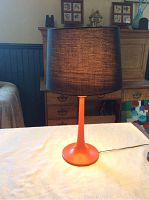 Full view of the lamp showing orange tulip base and black linen shade on a table.