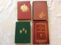 Four hardcover books laid out on fabric background showing front covers: Departmental Ditties by Rudyard Kipling (reddish-brown cover), two red covers including Alice's Adventures in Wonderland, and a green cover book.