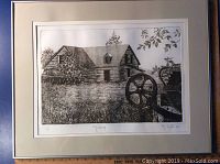 Framed black and white block print showing a rustic cabin with farm equipment in foreground.