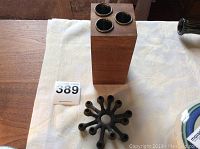 Two mid century candle holders on a white cloth background: a wooden block triple holder and a black starburst metal holder.